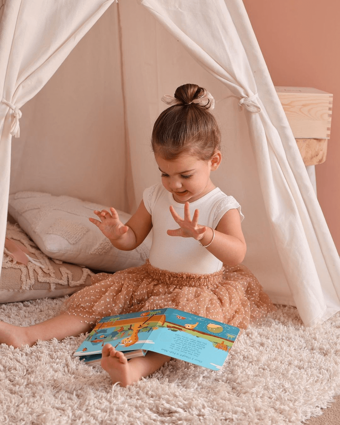 A young girl sits cross-legged in a play tent, reading Ditty-Bird AUS's Animal Songs, a colorful, interactive musical book with animal pictures that's USB-C rechargeable.