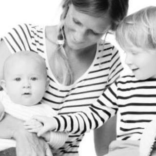 A woman holds a baby while a young child—both in striped shirts—gently touches the baby. Their smiles capture an affectionate moment, perfect for early learning and exploration with baby toys 6-12 months.